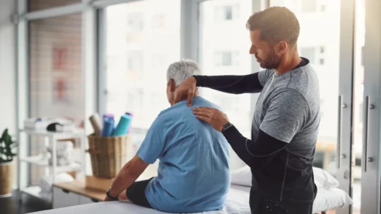 Un homme effectue une séance de thérapie physique avec un homme âgé, mettant en pratique des techniques d'ostéopathie.