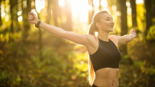 Une femme en brassière de sport s'étire les bras sous le soleil, profitant de la chaleur et de l'énergie extérieure.